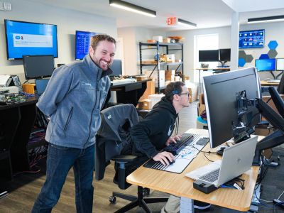 Man smiling while a technician works at his computer